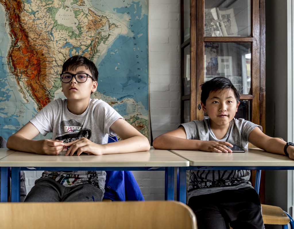 Klaslokaal met twee kinderen aan een tafeltje, voor een wereldkaart